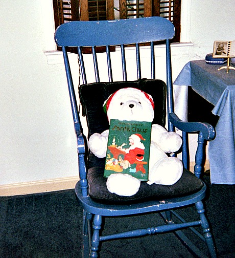 Stuffed bear in a rocking chair holding a book.